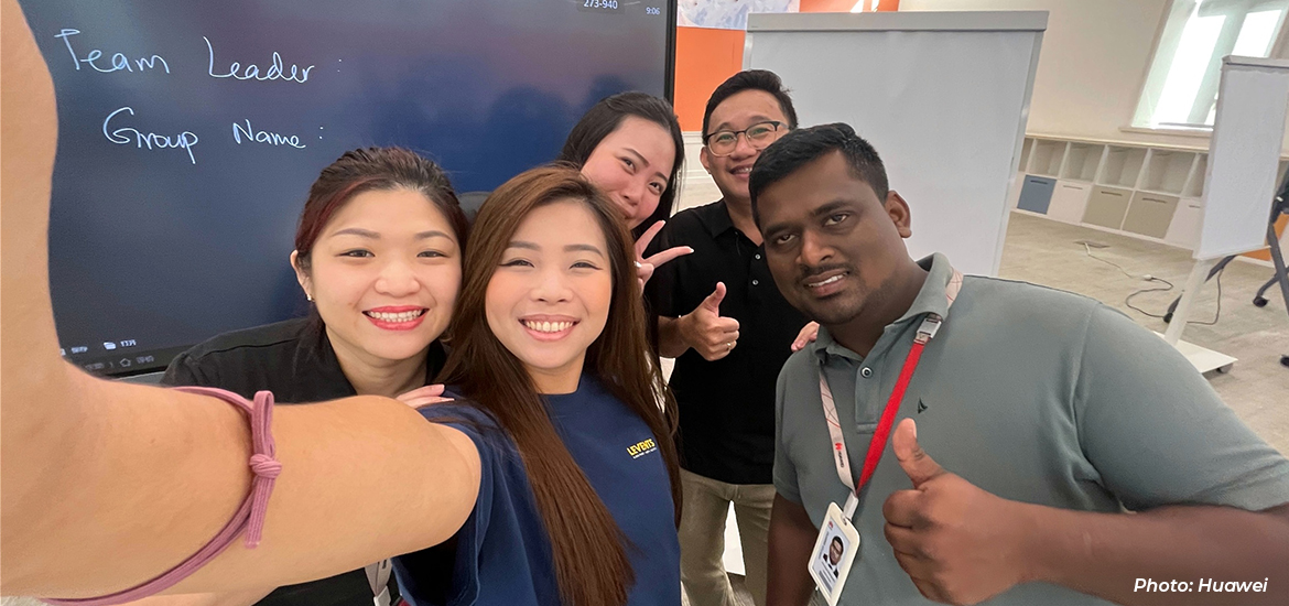 Group selfie of Huawei employees participating in a team-building or workplace training session, smiling and posing together in a collaborative office environment.