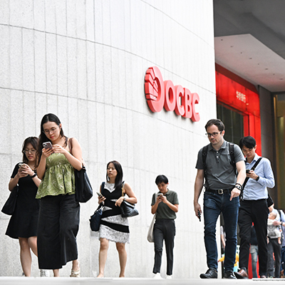 People walking past the OCBC building in Singapore’s central business district, many looking at their mobile phones while commuting.