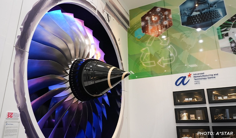 Close-up view of a large jet engine turbine displayed at the Advanced Remanufacturing and Technology Centre (ARTC), with colorful lighting and technology exhibits in the background.