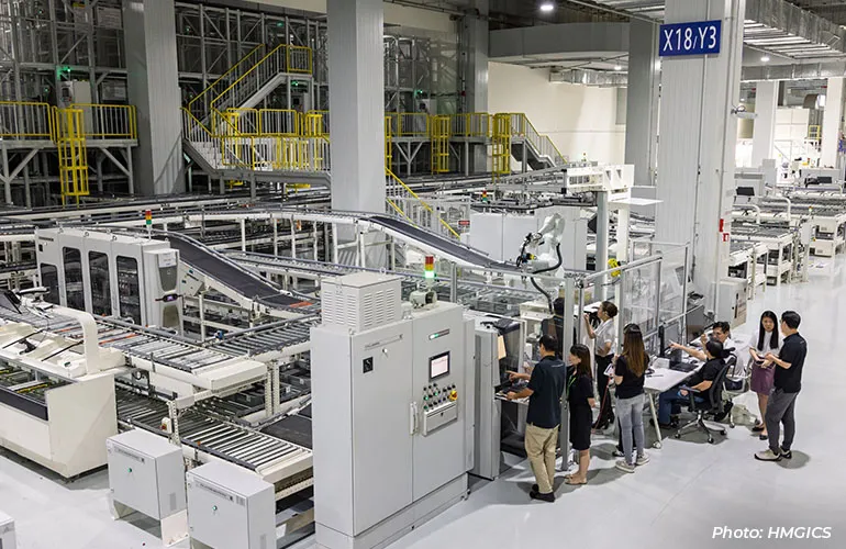 Engineers observing and operating an automated manufacturing line inside a large industrial production facility.