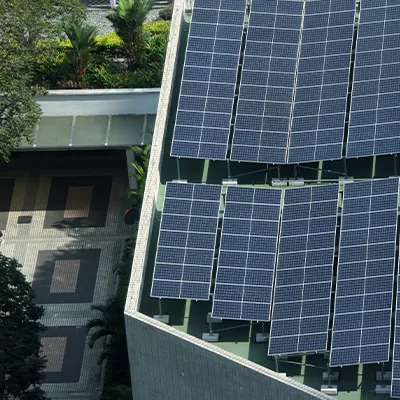 Aerial view of rooftop solar panels installed on a modern building, with two people walking on a patterned walkway below surrounded by trees.