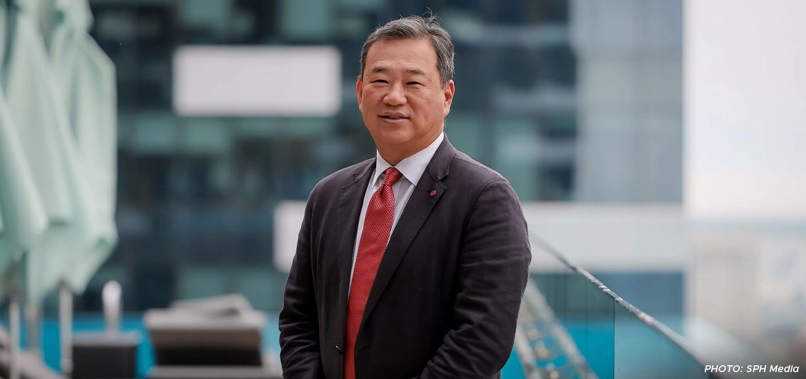 Lotte Retail Group vice-chairman and group CEO Sanghyun Kim smiling while standing outdoors on a balcony with modern glass buildings in the background.