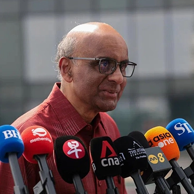 Man speaking to reporters at a media briefing with multiple microphones in front of him.