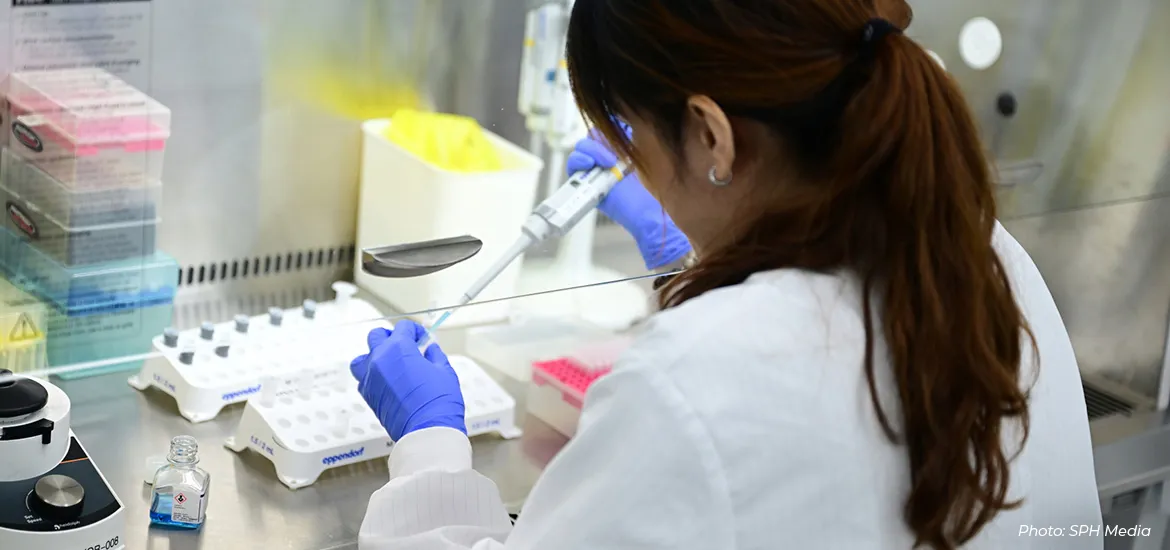 Scientist in a lab coat and gloves using a pipette for experiments in a laboratory setting.