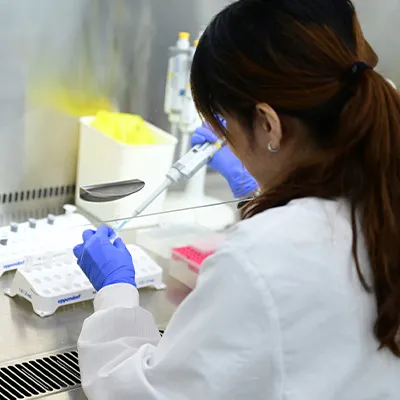 Scientist in a lab coat and gloves using a pipette for experiments in a laboratory setting.