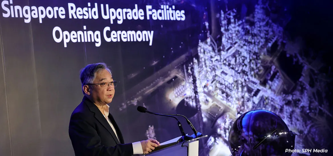 Man speaking at a podium during the Singapore Resid Upgrade Facilities opening ceremony, with an illuminated industrial facility backdrop.