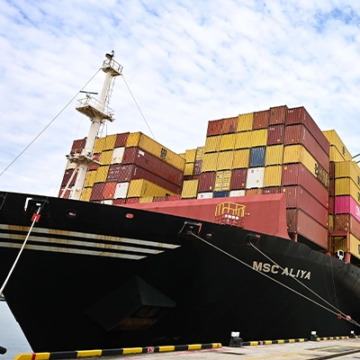 Large container ship MSC Aliya docked at a Singapore port, stacked with multicoloured shipping containers as gantry cranes load and unload cargo, highlighting Singapore’s role as a global maritime and logistics hub.