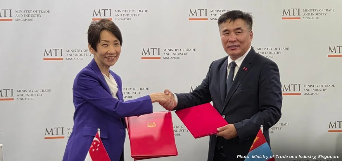 Representatives from Singapore’s Ministry of Trade and Industry and another country shaking hands after signing an agreement, holding red folders in front of an MTI backdrop.