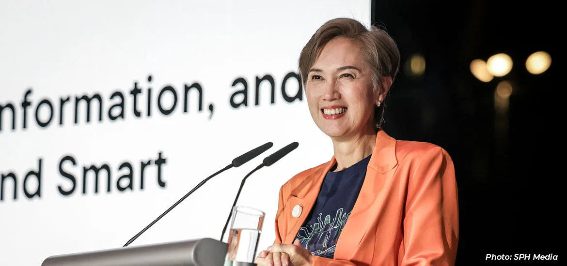 Smiling woman speaking at a podium during a conference, with presentation text in the background.