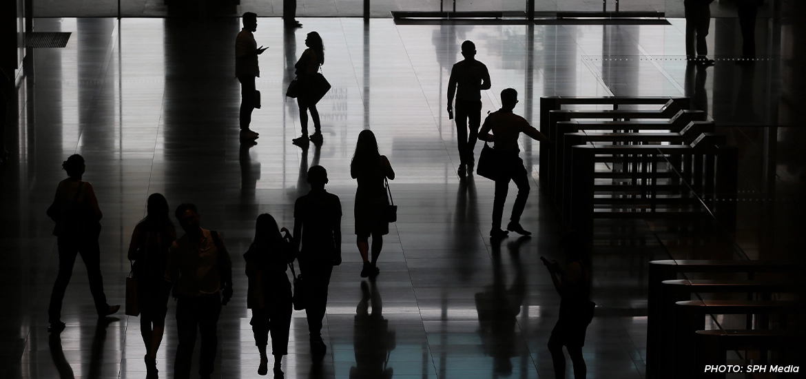 Silhouettes of people walking through a modern office building lobby with reflective floors.