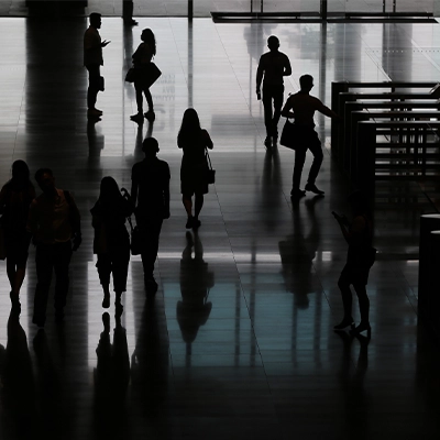 Silhouettes of people walking through a modern office building lobby with reflective floors.