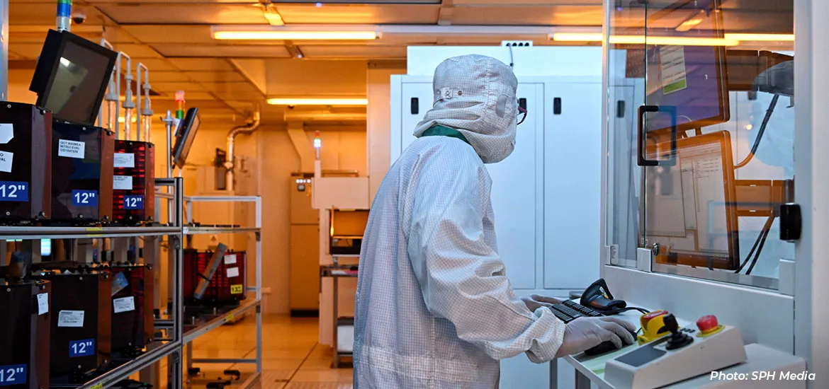 Technician in a cleanroom suit operating semiconductor manufacturing equipment inside a fabrication facility.