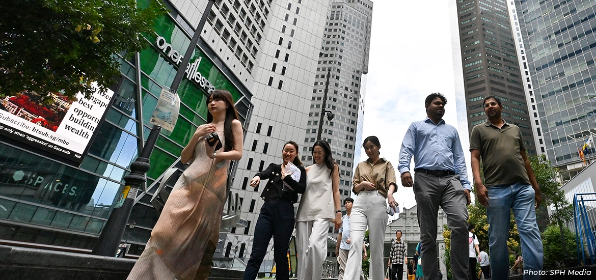 Group of professionals walking along a busy downtown street lined with modern skyscrapers, representing Singapore’s diverse workforce and vibrant central business district.