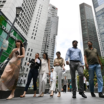 Group of professionals walking along a busy downtown street lined with modern skyscrapers, representing Singapore’s diverse workforce and vibrant central business district.