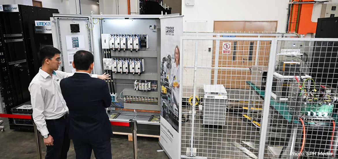 Two engineers reviewing an electrical control panel in an industrial facility.
