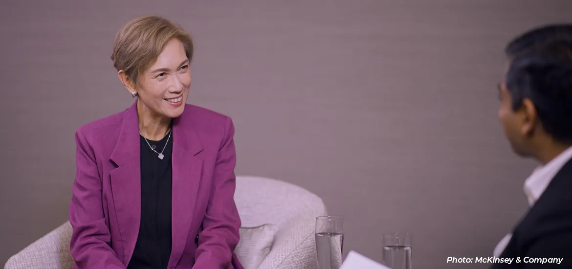 Woman in a purple blazer smiling during an interview, with a McKinsey & Company logo in the background.