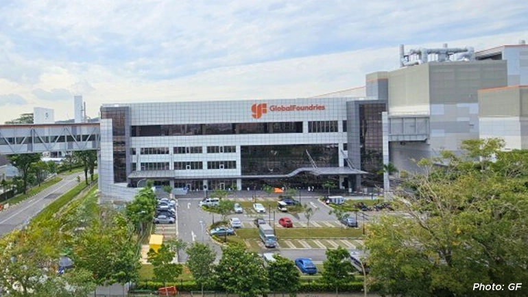 Aerial view of the GlobalFoundries semiconductor manufacturing facility in Singapore, featuring large modern factory buildings surrounded by greenery and roads.