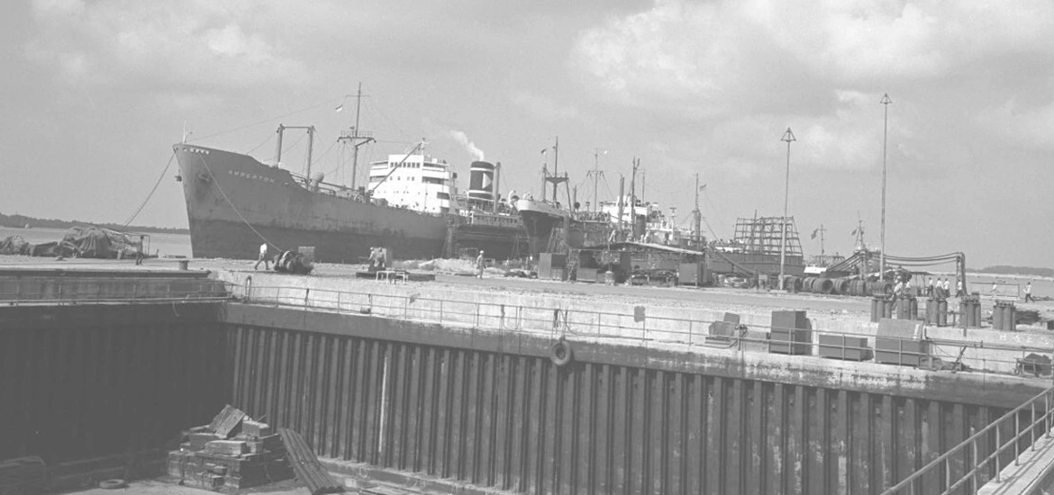 Black-and-white historical photo of a cargo ship docked at a port.