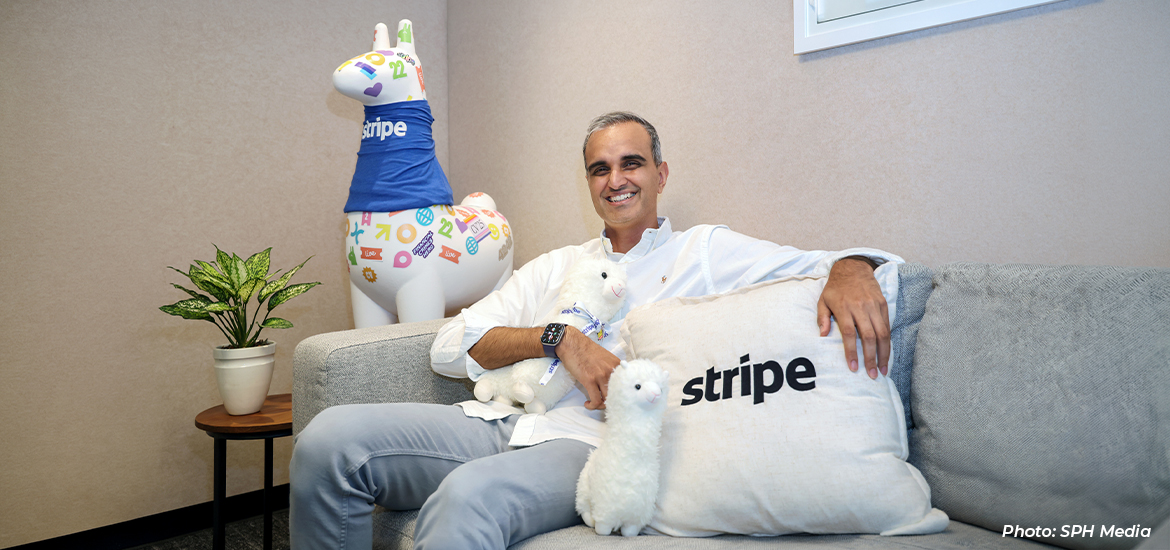 Portrait of a Stripe executive seated in a lounge area with branded décor and plush mascots, smiling in a relaxed office environment that reflects the company's workplace culture.