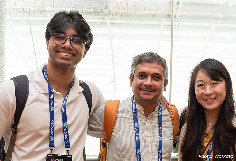 Three smiling attendees wearing Workato lanyards pose for a photo together at an event