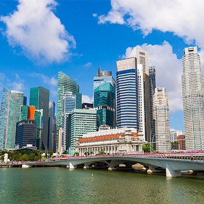 Singapore city skyline with high-rise buildings and a bridge over Marina Bay under a blue sky.