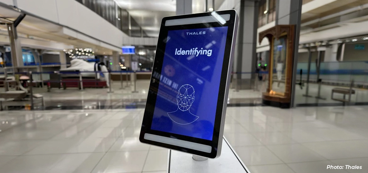 Tablet displaying a facial recognition identification screen in an airport terminal, with security screening area in the background.
