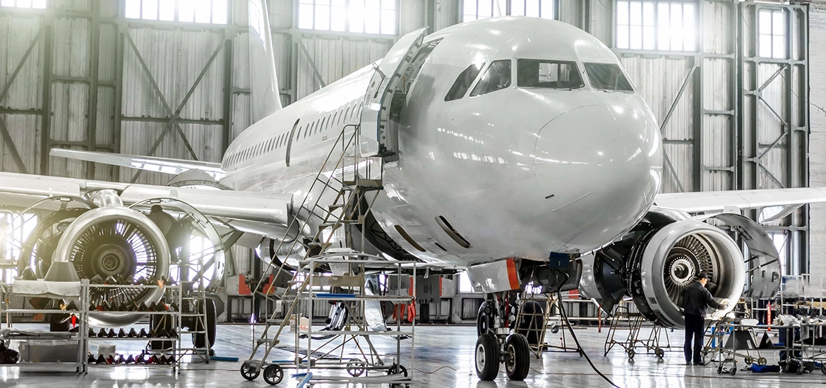 Aircraft undergoing maintenance in a hangar, with engineers working on its engines and systems.