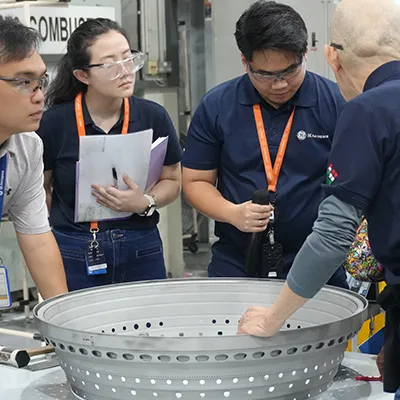 GE Aerospace engineers and technicians wearing safety glasses collaborate on the factory floor, reviewing a large aircraft component during hands-on training and advanced aerospace manufacturing operations.