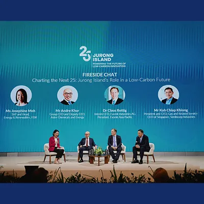 Panel discussion titled “Fireside Chat: Charting the Next 25 – Jurong Island’s Role in a Low-Carbon Future,” with four speakers seated on stage beneath a large screen displaying their names and titles.
