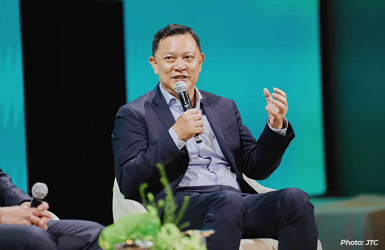 Man in a suit speaking into a microphone while seated on stage during a panel discussion.