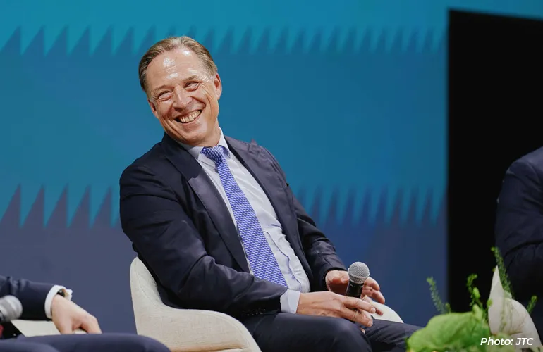 Man in a suit smiling while holding a microphone during a panel discussion on stage.