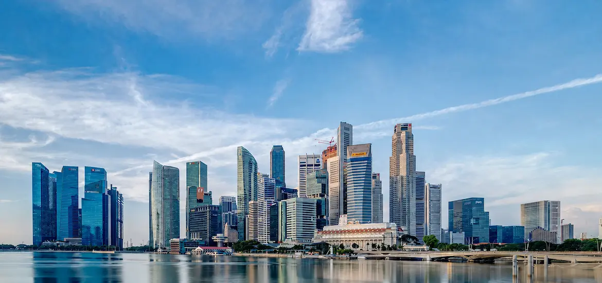 Singapore city skyline across Marina Bay under a blue sky.