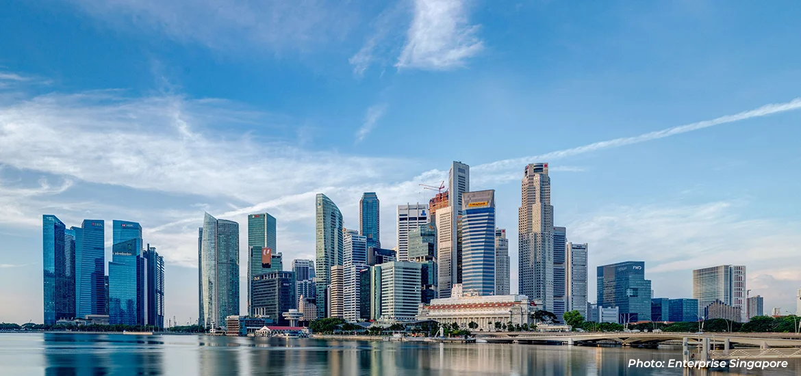 Singapore city skyline across Marina Bay under a blue sky.