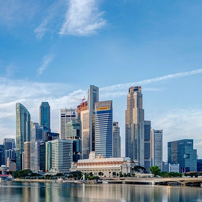 Singapore city skyline across Marina Bay under a blue sky.