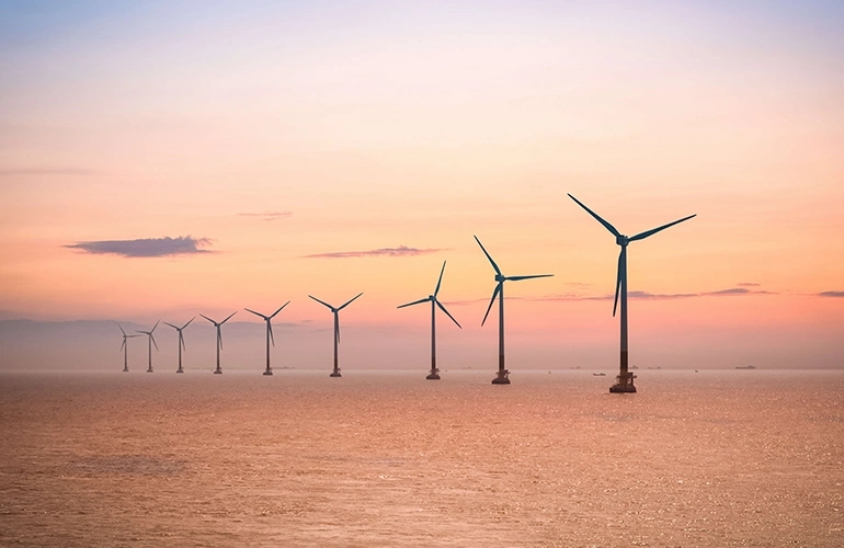 Offshore wind turbines at sea during sunset.