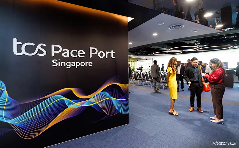 Interior of TCS Pace Port Singapore with a large branded wall on the left and professionals networking and conversing in a modern event space on the right.
