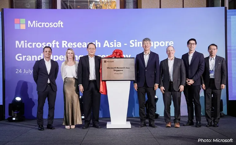 Microsoft executives and partners pose on stage at the Microsoft Research Asia – Singapore grand opening ceremony, standing behind a podium with a commemorative plaque and event backdrop.