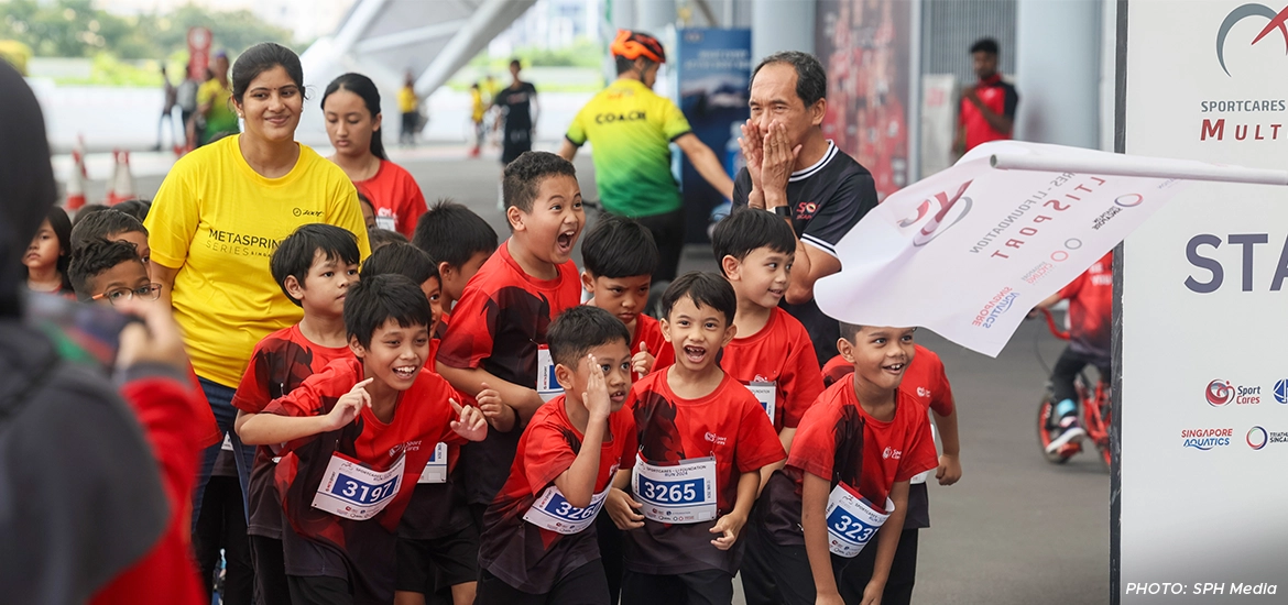 Excited children in red sports jerseys lined up at the starting line of a race, smiling and ready to run.