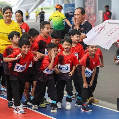 Excited children in red sports jerseys lined up at the starting line of a race, smiling and ready to run.