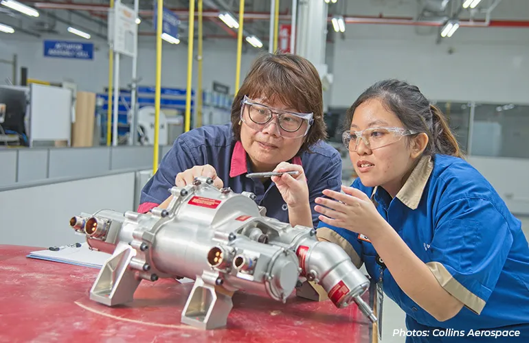 Two engineers examine and discuss a metal industrial component in a factory workshop.