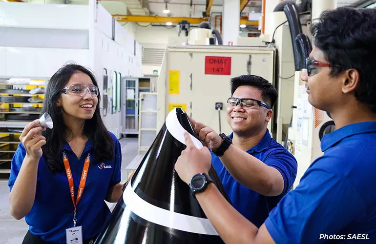 Three factory workers inspect and discuss a large manufactured component on the shop floor.