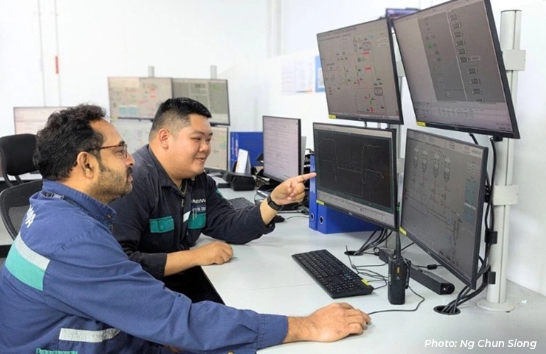 Two technicians reviewing data on multiple computer monitors at a workstation.