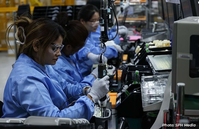 Workers wearing protective eyewear and cleanroom attire assembling electronic components on a production line in a manufacturing facility.