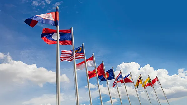 Row of Southeast Asian national flags waving against a blue sky, symbolizing regional unity, cooperation, and international partnerships.