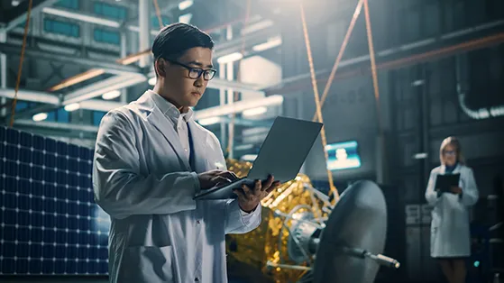 Engineer in lab coat working on a laptop in a space technology facility, symbolizing advancements in the space sector.