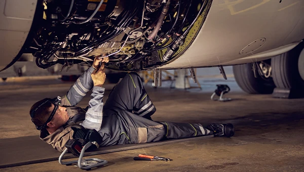 Aerospace technician performing maintenance under an aircraft, symbolizing precision engineering, safety, and cutting-edge capabilities in the aviation industry.
