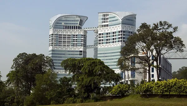 Modern research facility with two uniquely designed high-rise buildings connected by skybridges, surrounded by lush greenery.
