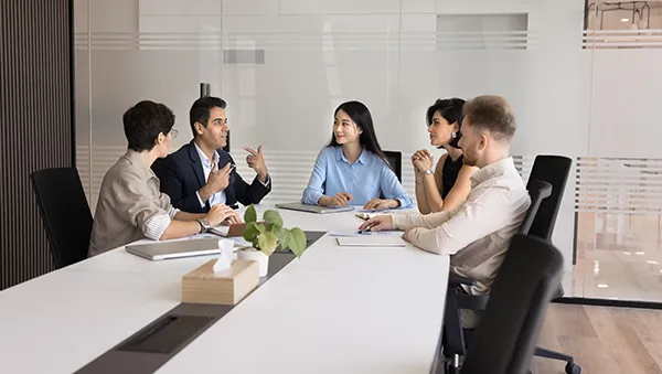 Group of diverse professionals having a discussion around a conference table in a modern office meeting room.