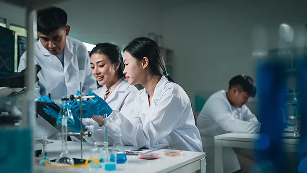 Young scientists in lab coats collaborating on an experiment in a modern laboratory equipped with glassware and microscopes.