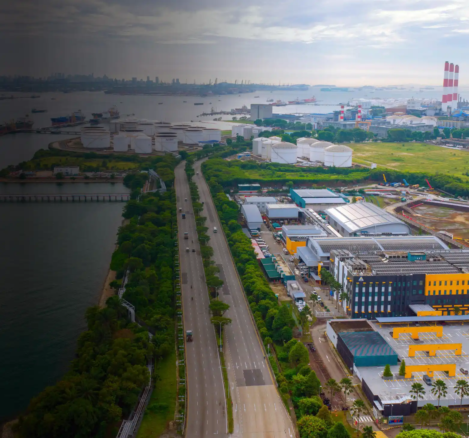 Aerial view of a coastal industrial area with oil storage tanks, port facilities, ships, and power plant chimneys along the waterfront.